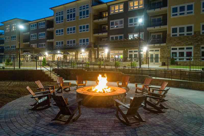 Adirondack chairs surround Lakeside Lodge's firepit, where an orange flame flickers beneath the evening sky.